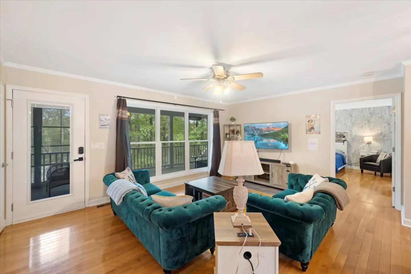 Open-concept living room with teal sofas, hardwood floors, and tall windows to the lake