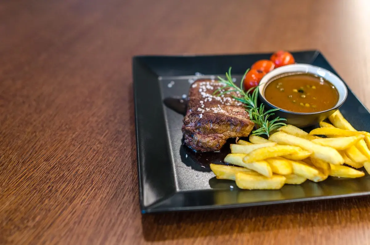 Grilled steak with fries, tomatoes, and sauce on a dark plate
